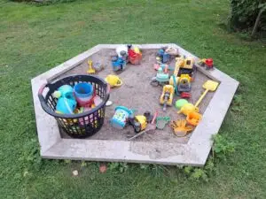 Sandlåda fylld med leksaksfordon och hinkar på gräsmattan